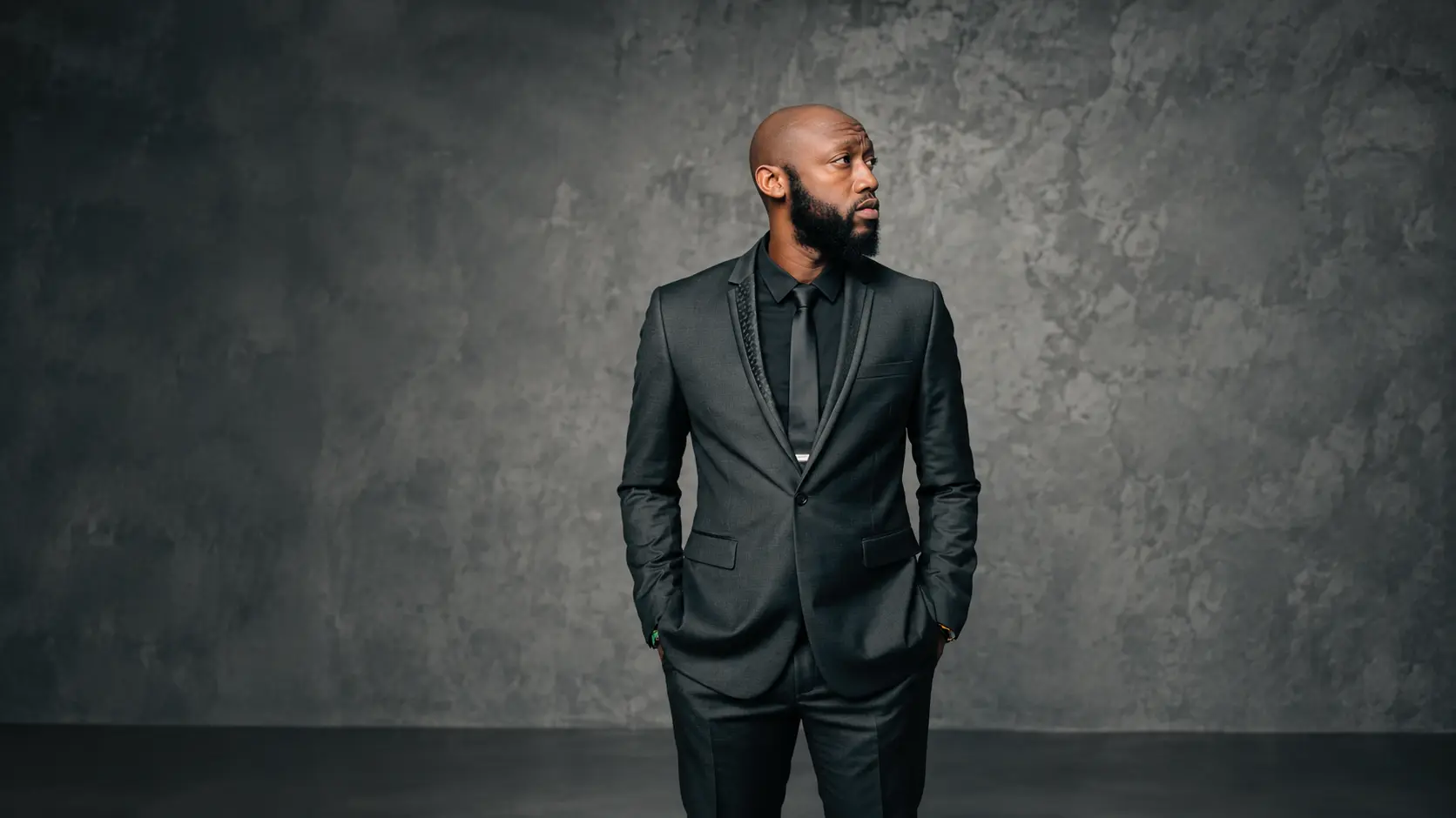 Dee Bright Jr. in a black suit against a charcoal wall